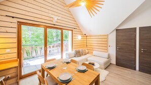 A modern loft-style room with a dining area, a sofa, and a large sliding glass door to a balcony. - “L’aubier des Bauges” Apartment: Mountain View, Private Terrace, Wi-Fi (Les Déserts)