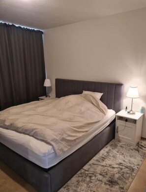 A bedroom with a bed, a nightstand, a lamp, and a window with curtains. - Serene 3-bedroom apartment in Reykjavík perfect for your getaway (Reykjavík)