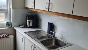 Pieni keittokomero, jossa on valkoiset kaapit, ruostumattomasta teräksestä valmistettu pesuallas, kahvinkeitin ja vedenkeitin.