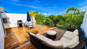 A wooden deck with wicker furniture, a table, chairs, and a grill. - Spacious 4 bedroom Oasis with Rooftop in PlayaCar (Playa del Carmen)