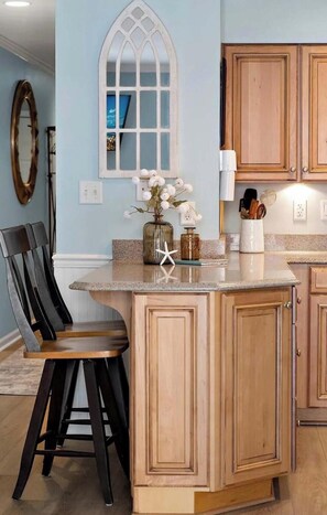 A kitchen with a central island, wooden cabinets, a bar stool, and a decorative window. - Outrigger 210 (Ocean City)