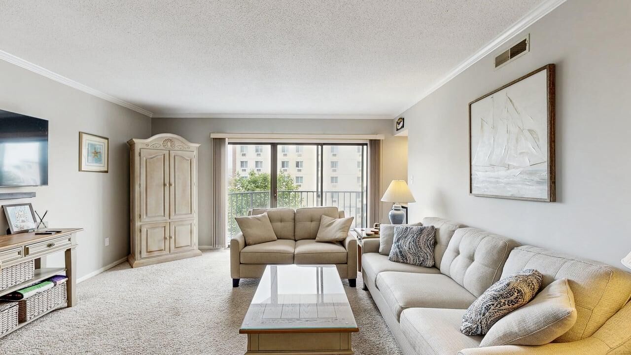 A living room with a sofa, a coffee table, a cabinet, a TV, and a window with a view of buildings.