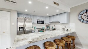 A modern kitchen with white cabinets, stainless steel appliances, a marble countertop, and a clock on the wall. - Royal Hawaiian 205 (Ocean City)