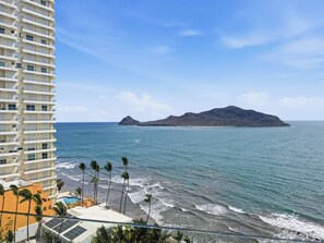 Küstensicht mit einem Hotel, Strand, Palmen und einer entfernten Insel.