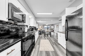 A modern kitchen with a built-in oven, microwave, and refrigerator, wooden flooring, and a dining area with chairs and a table. - All New! 3 Min To Strip! Year Round Pool, Hot Tub, Sauna! (Branson)