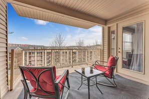Een overdekt balkon met een tafel en stoelen, en uitzicht op een woonwijk, met een deur voorzien van een raam.