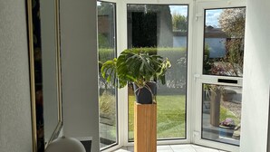 A room with a large window, a potted plant on a wooden stool, and a lamp on a side table. - Leling Holiday Apartment – Relaxation with a Wellness View (Havixbeck)