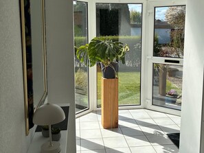Ein Zimmer mit großem Fenster, einem Blumentopf, einer Lampe und einem gefliesten Boden.