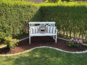 Eine weiße Bank mit gestreiften Kissen in einem angelegten Garten.