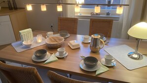 A dining table set with bowls, cups, and a kettle, surrounded by wicker chairs, with a lamp and candles on the table. - Leling Holiday Apartment – Relaxation with a Wellness View (Havixbeck)