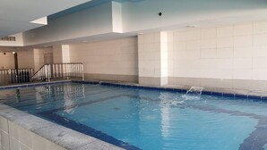 An indoor swimming pool with tiled walls and a clear blue pool. - Modern Comforts: Al Raha Beach modern 1 bedroom near AD airport (Abu Dhabi)
