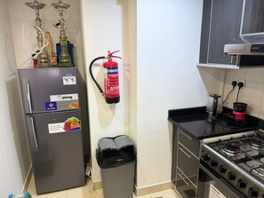 Eine Küche mit einem Kühlschrank, einem Gasherd, einem Mülleimer, einem Feuerlöscher und zwei Wasserpfeifen.