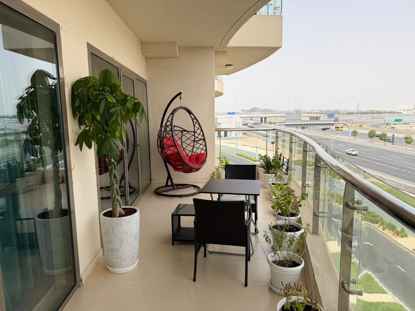 Ein Balkon mit Glastür, einer Hängematte, einem Tisch, Stühlen und Blumentöpfen.
