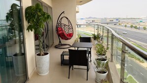 A balcony with a glass door, a hanging chair, a table, chairs, and potted plants. - Modern Comforts: Al Raha Beach modern 1 bedroom near AD airport (Abu Dhabi)