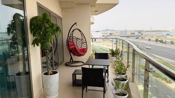 Ein Balkon mit Glastür, einer Hängematte, einem Tisch, Stühlen und Blumentöpfen.