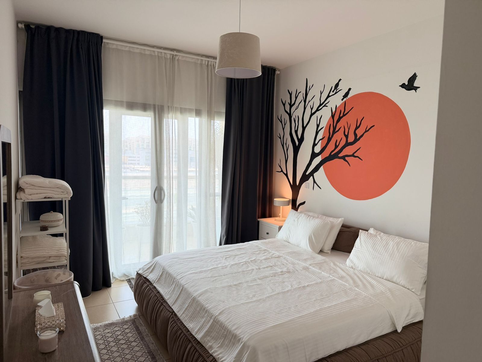 Ein Schlafzimmer mit einem Bett, einem Nachttisch, einer Lampe und einer Wandmalerei.