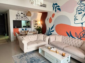 A living room with a sofa, a coffee table, and a dining area with chairs. - Modern Comforts: Al Raha Beach modern 1 bedroom near AD airport (Abu Dhabi)