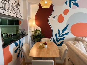 Ein Essbereich mit Holztisch, vier Stühlen, einem Topfpflanzen und einer Wand mit abstrakter Kunst.