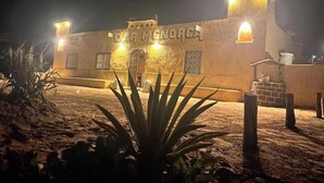 Un edificio con el letrero 'BAR MENORCA' de noche, con fachada de piedra y una pequeña estructura de ladrillo a la derecha.