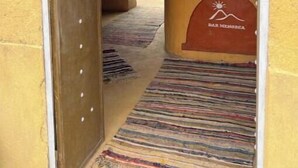 A doorway leading to a room with a patterned carpet, a reception desk with a logo, and a wall with framed pictures. - Riad Dar Menorca - Peaceful Desert Stay with Patio at the Foot of the Dunes (Merzouga)