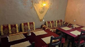 A restaurant with red velvet-covered tables and matching chairs, a wall-mounted light fixture, and decorative wall patterns. - Riad Dar Menorca - Peaceful Desert Stay with Patio at the Foot of the Dunes (Merzouga)