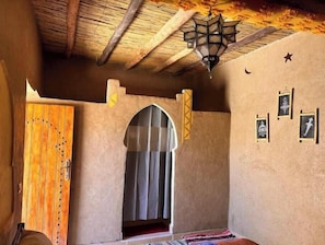 A room with a wooden door, a window with a curtain, a hanging lantern, and wall-mounted pictures.