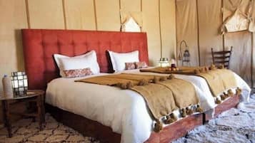A bed with a red headboard, white bedding, and a wooden footboard. There is a small table with a lamp and a chair beside the bed.
