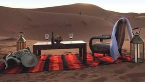 Eine Wüstenlandschaft mit einem Tisch für zwei Personen, einem Stuhl, einer Decke und zwei Laternen.