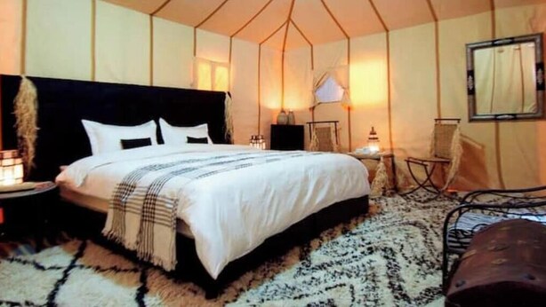 A tent-style bedroom with a bed, bedside lamps, a chair, and a rug.