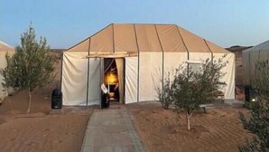 A large tent with a central doorway, surrounded by a sandy area with sparse vegetation.