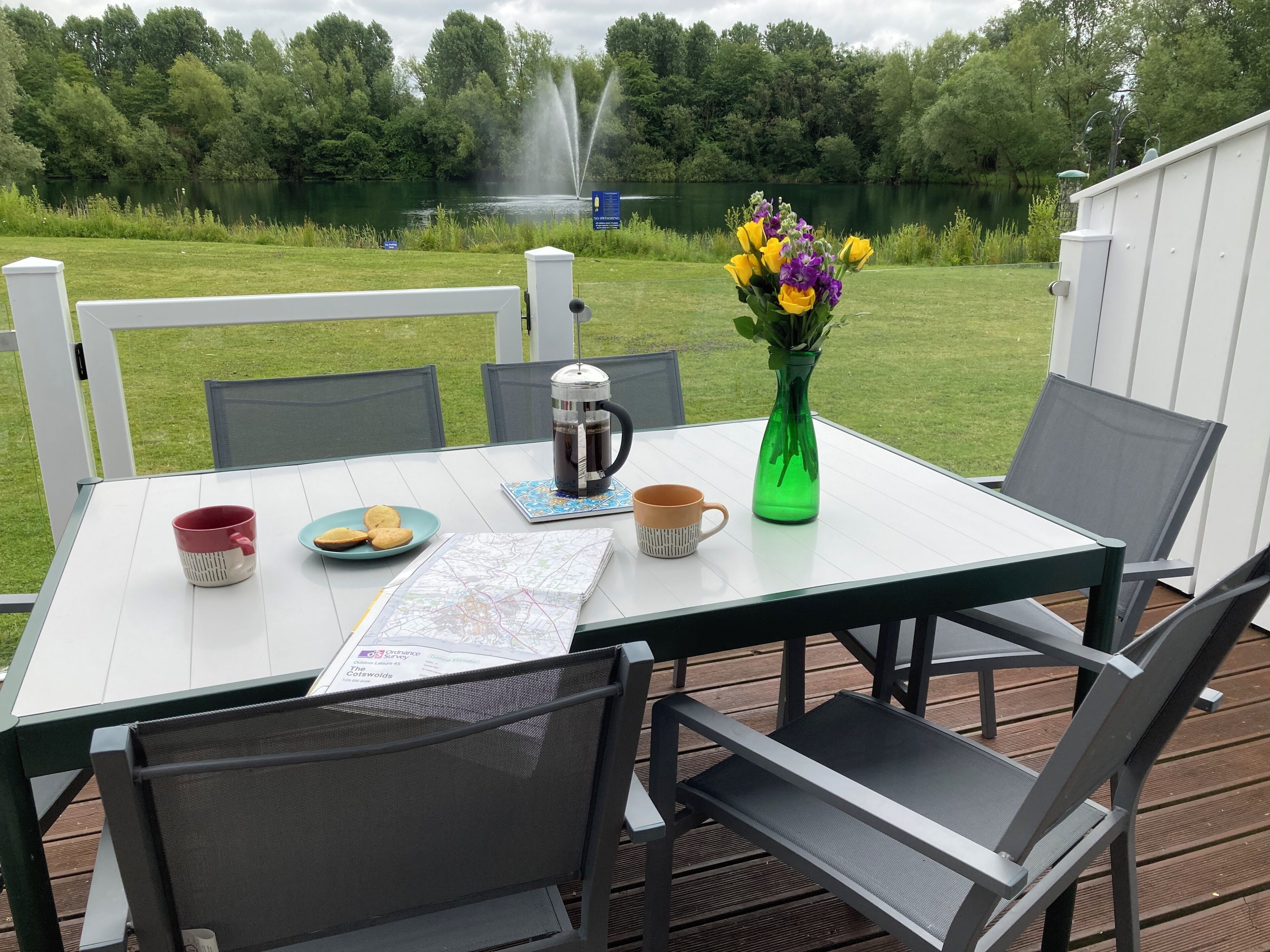 Une table avec une carte, une cafetière, une tasse, des biscuits et un vase rempli de fleurs.