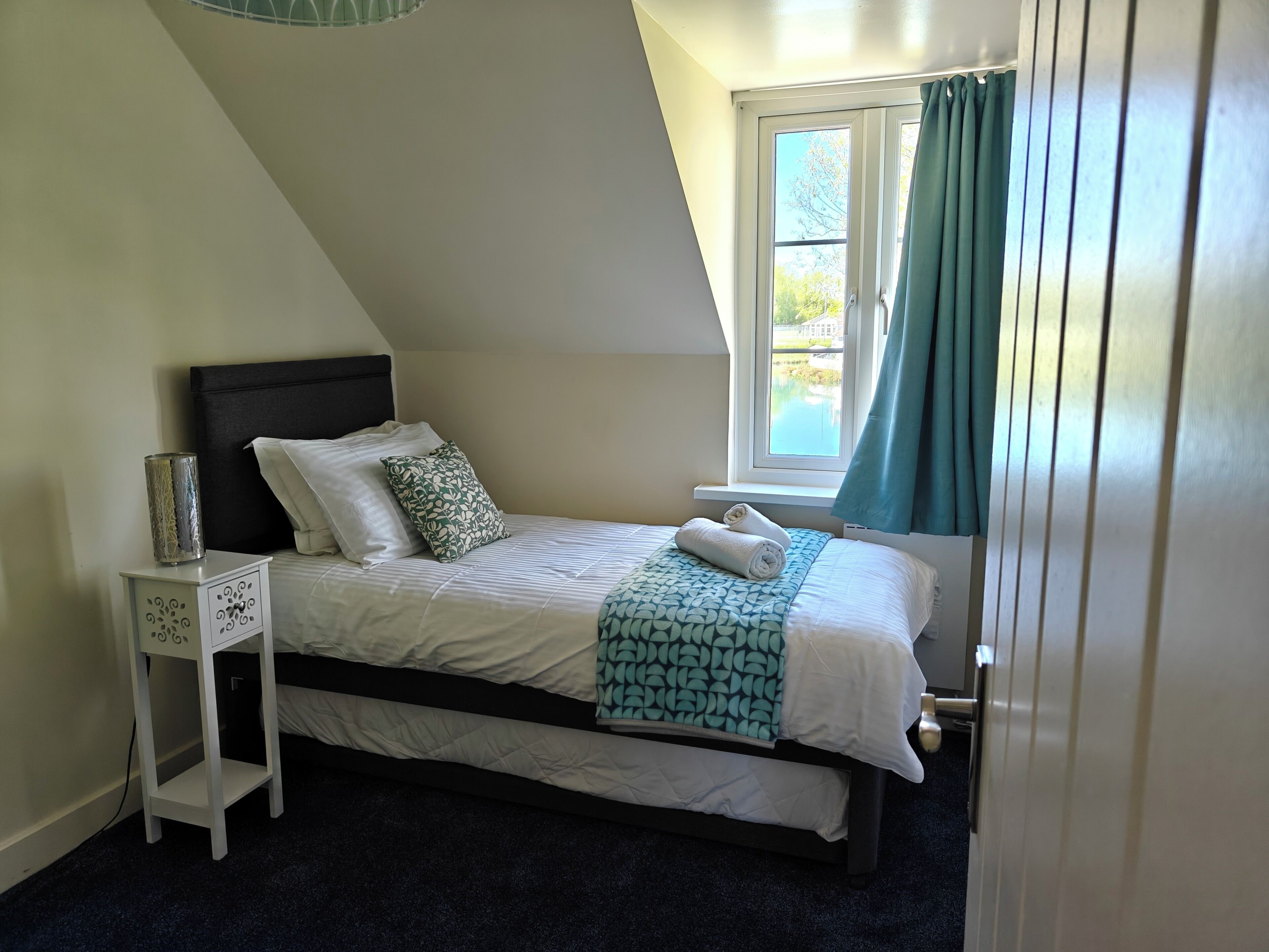 Une chambre à coucher avec un lit, une table de chevet, une fenêtre avec des rideaux et une vue sur l’extérieur.