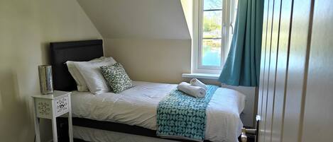 Une chambre à coucher avec un lit, une table de chevet, une fenêtre avec des rideaux et une vue sur l’extérieur.