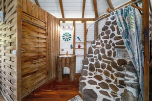 A rustic bathroom with wooden walls, a stone accent wall, a wooden floor, a sink, and a shower area. - Bungalow Yuka, a refuge between sea and nature (Les Anses-d'Arlet)