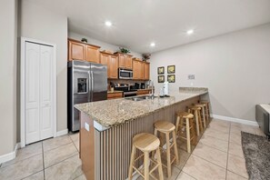 A modern kitchen with a granite countertop, stainless steel appliances, wooden cabinets, and a bar area with stools. - 4BR house with private pool in Storey Lake (Kissimmee)