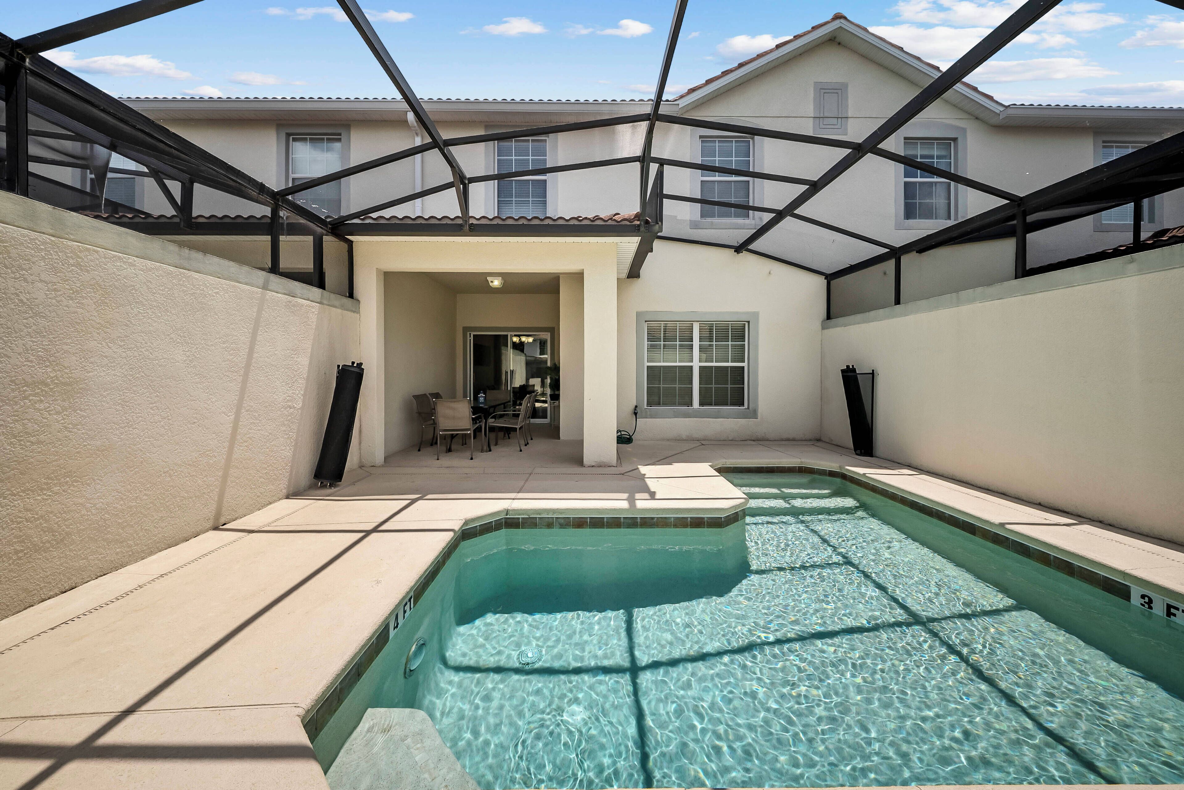 Una piscina con superficie d'acqua cristallina e blu, circondata da un portico coperto con vista su una casa sullo sfondo.