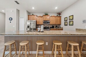Eine moderne Küche mit einer zentralen Kochinsel, Barhocker, Edelstahlgeräten und Holzschränken.