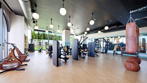 Un gimnasio con equipo de ejercicio, sacos de boxeo y grandes ventanales.