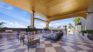 Zona exterior con mobiliario de lounge, mesas y piso a cuadros, con vista a un paisaje urbano.