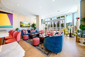 Eine moderne Hotellobby mit einer Sitzecke, einem Esstisch und einem großen Fenster mit Blick ins Freie.