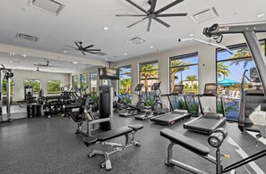 Ein Fitnessstudio mit verschiedenen Trainingsgeräten, großen Fenstern und Deckenventilatoren.