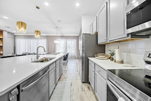 A modern kitchen with stainless steel appliances, a large island, and pendant lighting. - 8BR house sleeps 17 with pool table (Orlando)