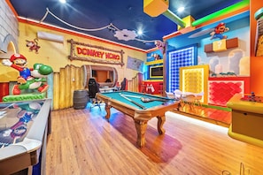 Ein Billardtisch in einem Raum mit Mario- und Luigi-Dekoration, einem 'Donkey Kong'-Schild und Holzboden.