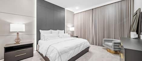 A modern bedroom with a large bed, bedside tables, a desk, and a chandelier.