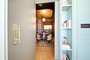 Ein Korridor führt zu einem Essbereich mit einem runden Tisch, Stühlen, einem gemusterten Boden und einem Bücherregal mit Büchern und einer Trophäe.