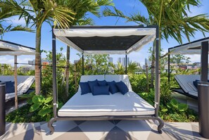 A bed with a canopy, surrounded by greenery, with a cityscape in the background. - Apartment at Nomad Residences Wynwood with 2BR (Miami)