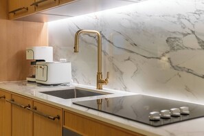 A kitchen with a marble backsplash, a gold faucet, a coffee maker, and a black induction cooktop. - At Nomad Residences wynwood: 2BR apartment (Miami)