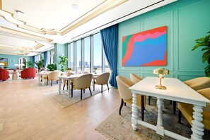 Eine Hotelhalle mit modernem Design, ausgestattet mit einem großen Fenster, einem farbenfrohen abstrakten Gemälde und unterschiedlichen Sitzgelegenheiten.