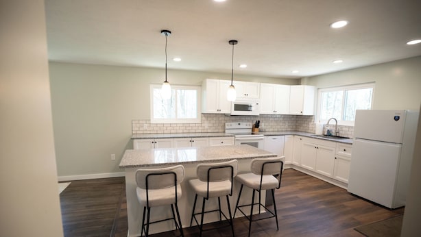 A modern kitchen with white cabinets, a granite countertop, and a central island with bar stools. - Secluded 5BR Retreat w/ Hot Tub, Sleeps 10 (Canfield)