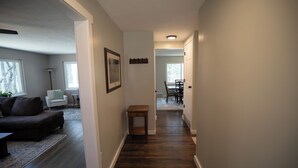 A hallway with a dark wood floor, a small table, a chair, and a dining area in the distance. - Secluded 5BR Retreat w/ Hot Tub, Sleeps 10 (Canfield)